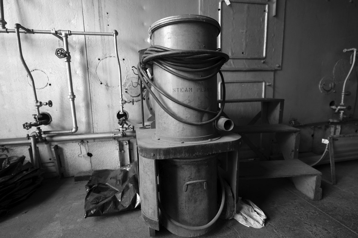 A black and white photograph of a water heater and pipes in a basement