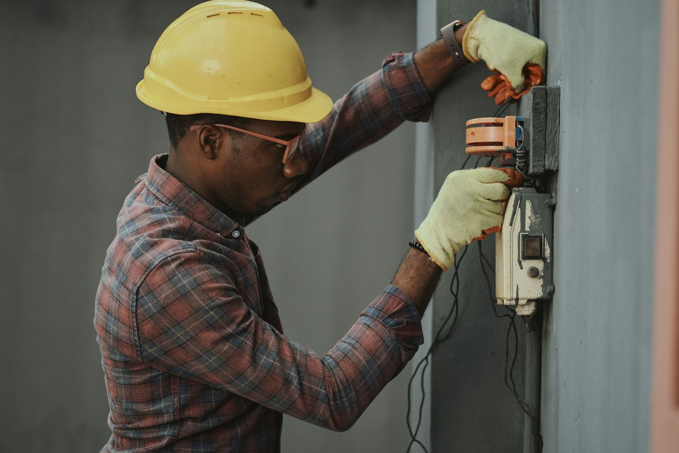 A worker in a hard hat and gloves checking equipment on a wall