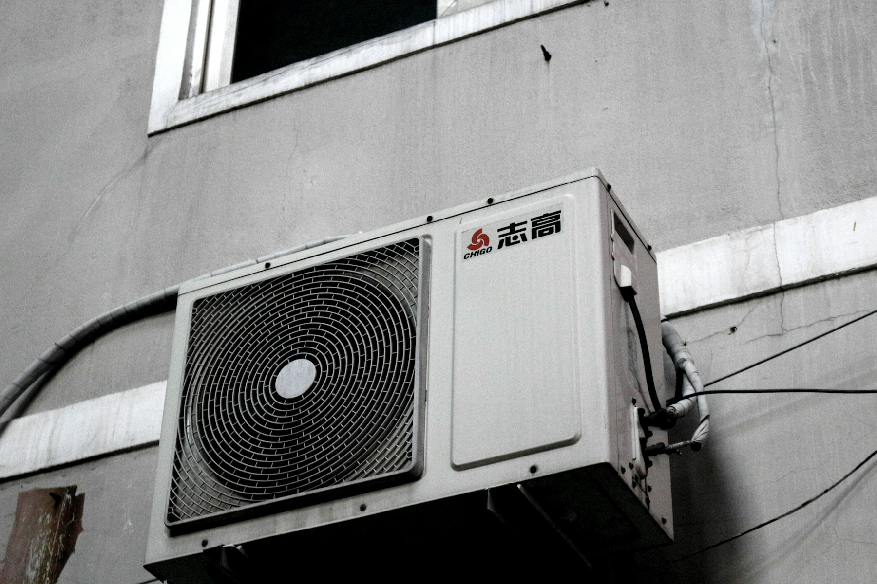 A black and white photograph of an air conditioner condenser mounted on a wall