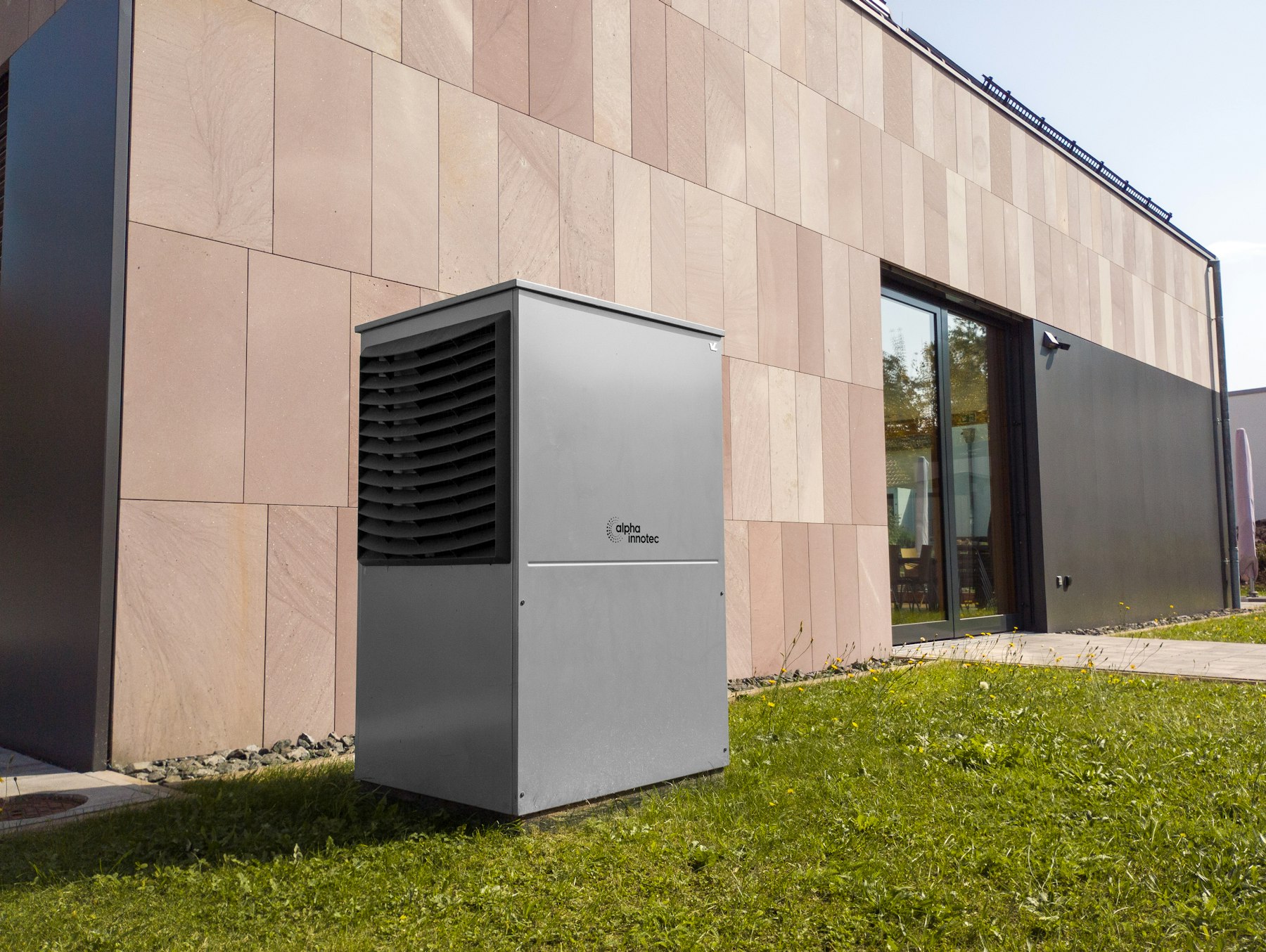 A tall grey heat pump outdoor unit standing on a lawn beside a modern house